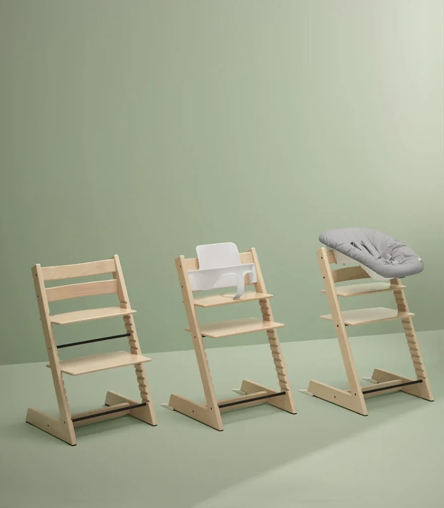 Three Stokke Tripp Trapp baby high chairs on a green background